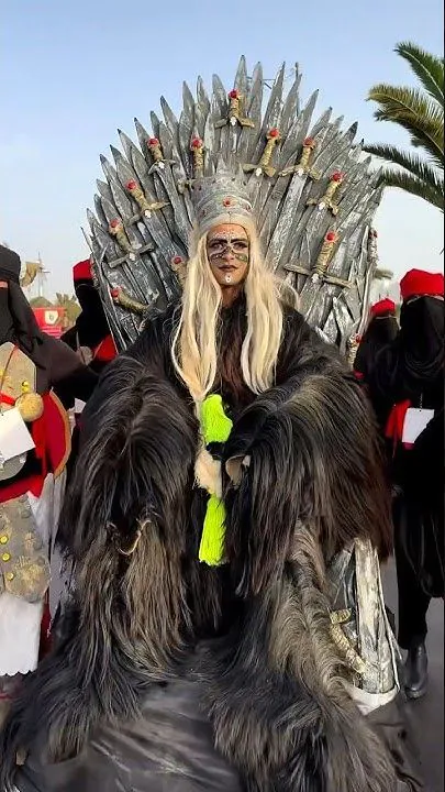 A young man dressed in a traditional Boujloud costume made of goat skin, wearing a handmade mask and holding a stick during a street parade in Agadir.